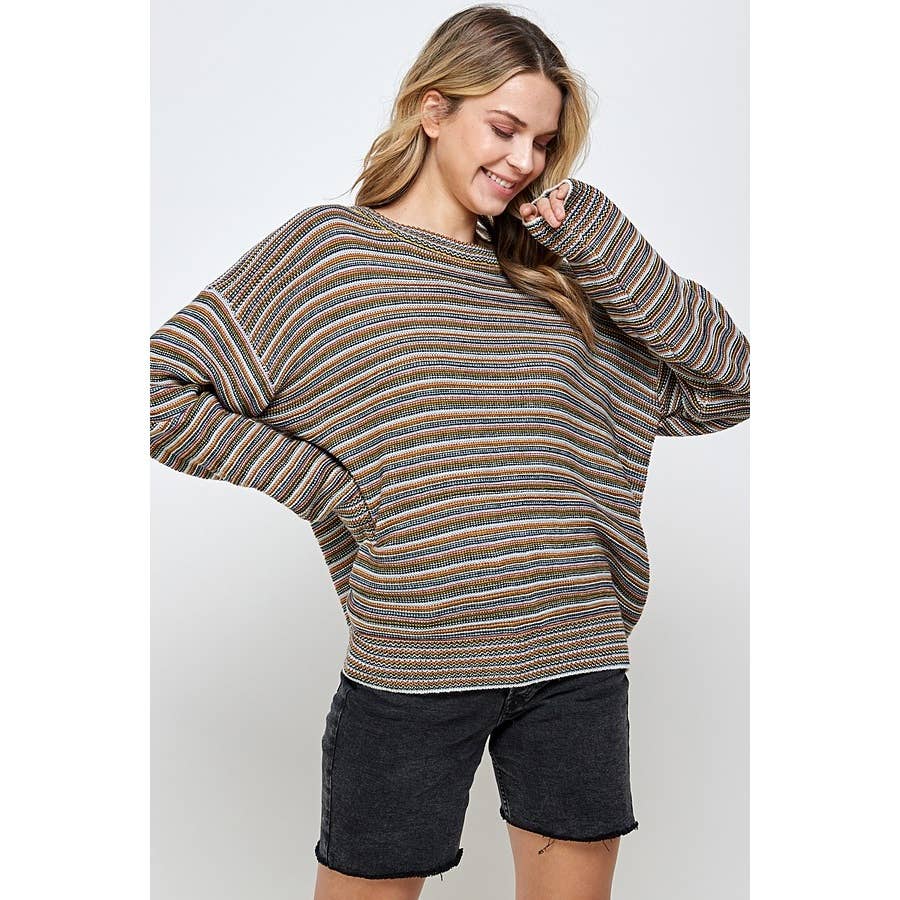 A person wearing a Sweet Generis Multi Color Stripe Pullover Sweater with an oversized, long-sleeved design in muted earth tones, paired with black denim shorts.