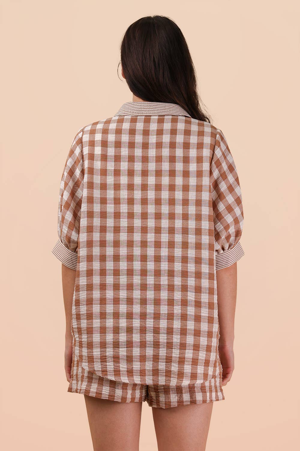 A person with long brown hair is facing away, wearing the VERY J Checkered Shirt Top & Shorts Set in brown and white. The background is a plain light beige color.