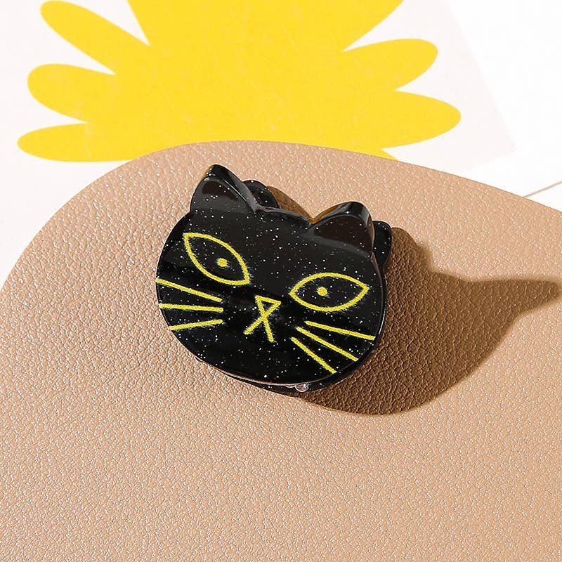 A set of four Halloween ghost-themed mini hair clips from JOSSLYN by wall to wall rests on a beige surface, with a yellow abstract shape visible in the background.
