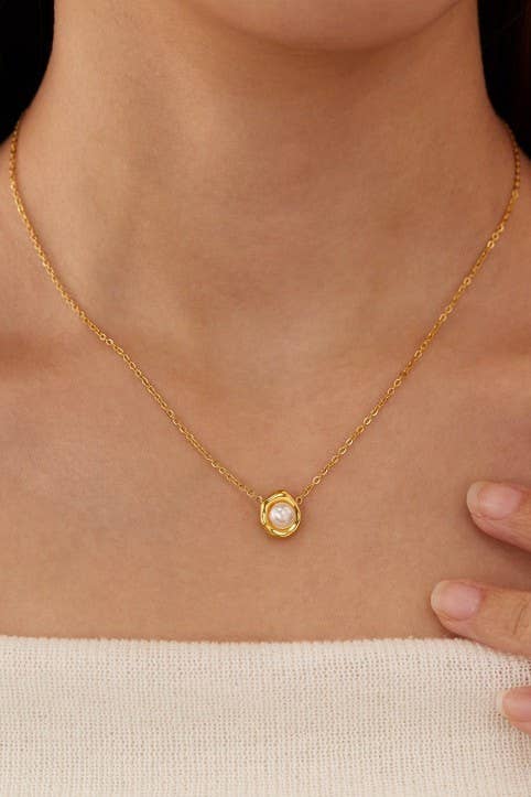 A close-up shows a person wearing the Tarnish Free Pearl Necklace by JOSSLYN by wall to wall, featuring a round pearl pendant on a gold chain that rests against their bare skin above a cream-colored top. One hand gently touches their shoulder.