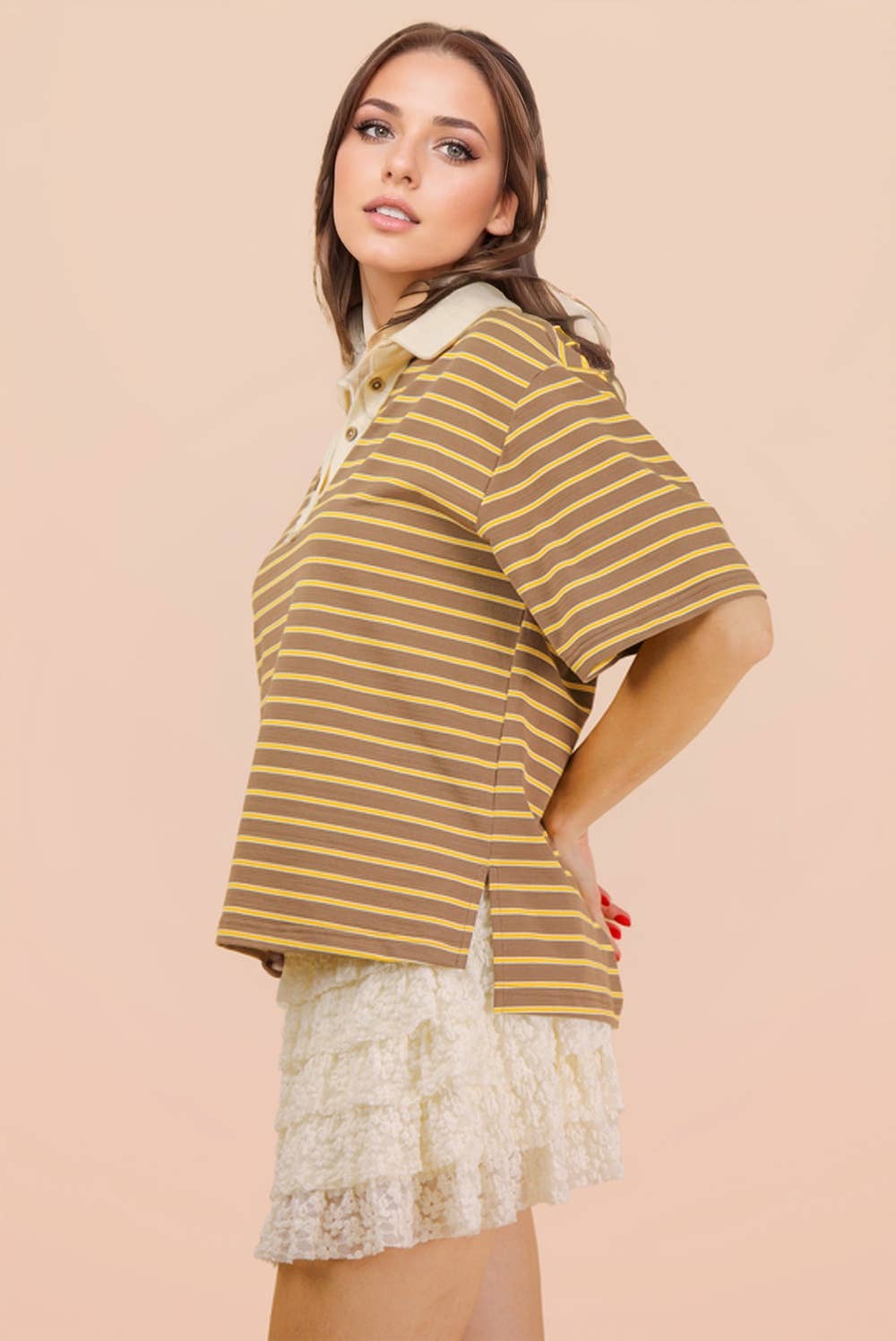 A woman wearing a Mocha Oversized Stripe Knit Top, a brown, yellow, and cream striped short-sleeve polo shirt with a buttoned collar and side slits.