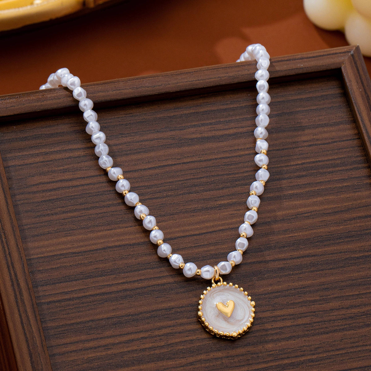 A JOSSLYN by wall to wall Pearl Beaded Heart Charm Necklace featuring a string of white pearls and gold beads with a circular pendant containing a small gold heart.