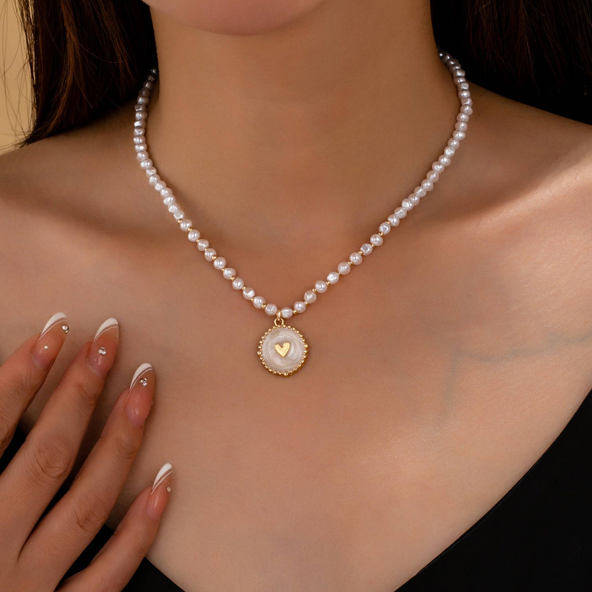 A JOSSLYN by wall to wall Pearl Beaded Heart Charm Necklace featuring a round pendant with a small gold heart in the center.