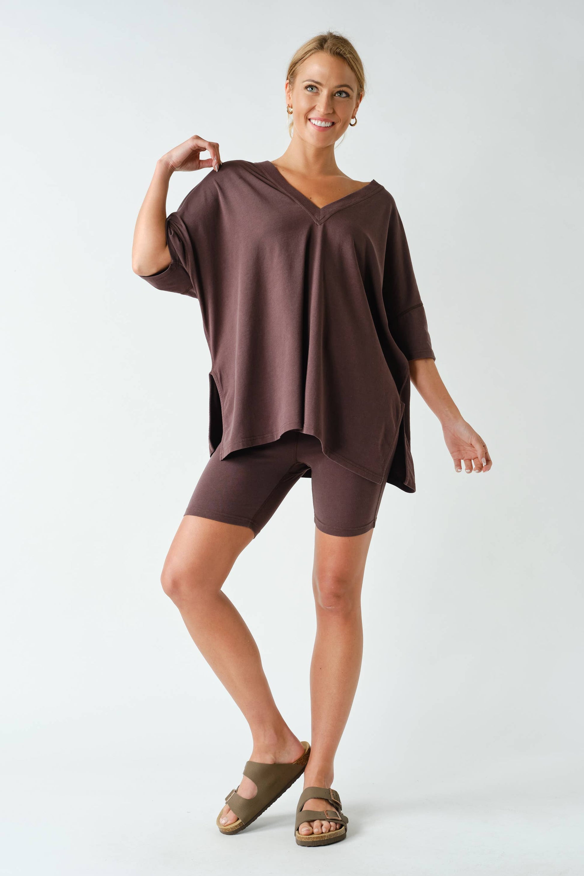 A woman stands smiling on one leg against a plain white background, dressed in the Switchback Pima Cotton Set by Mono B.