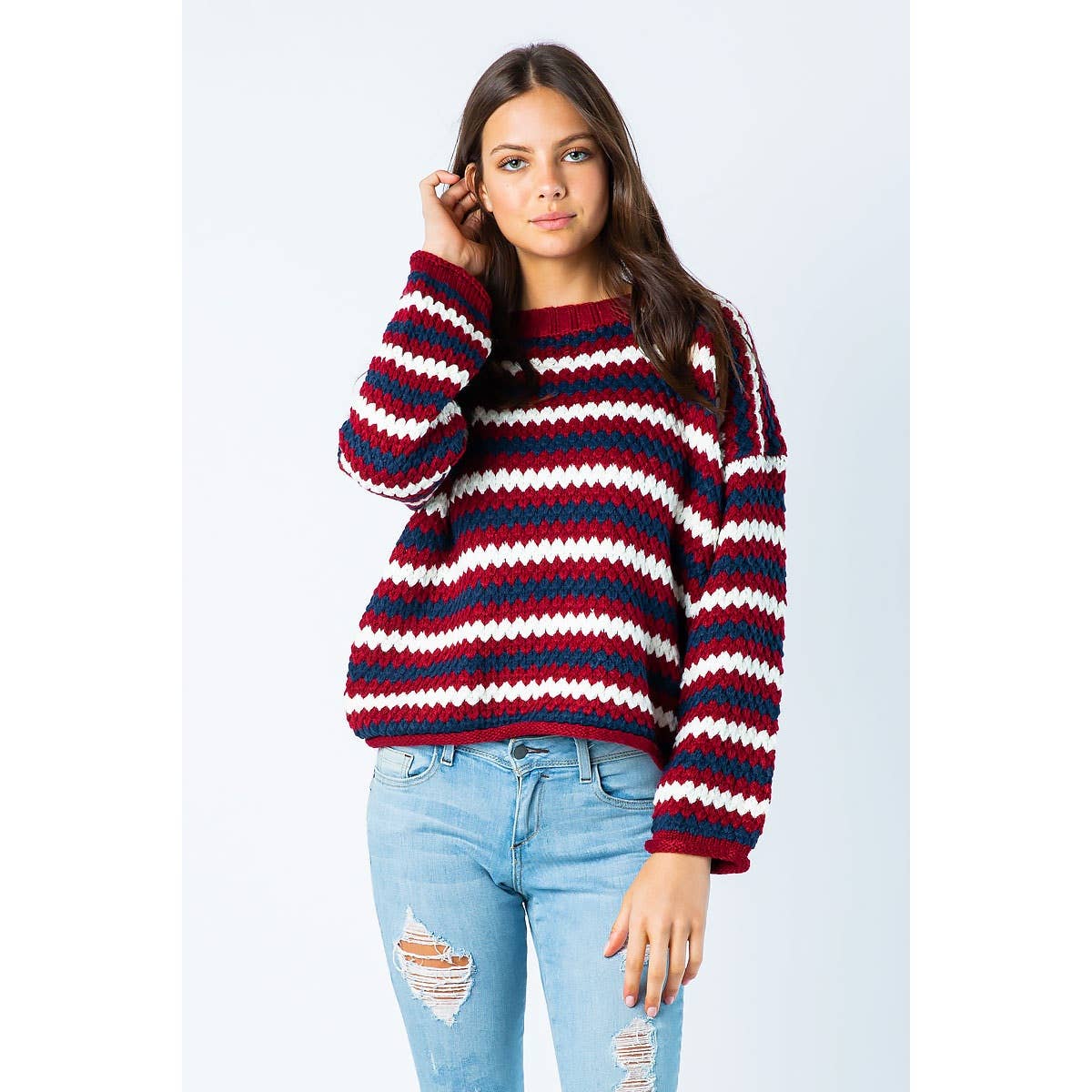 A woman wears a Sweet Generis Chunky Knit Multi Color Sweater featuring horizontal red, white, and blue zig-zag stripes.
