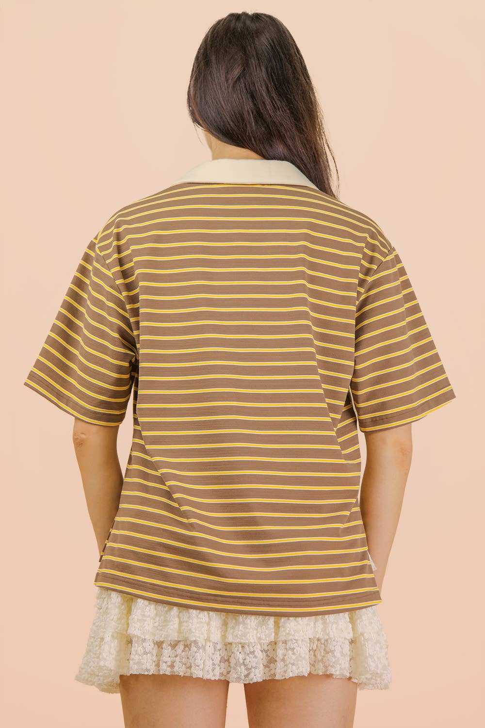 A person viewed from the back wearing a Mocha Oversized Stripe Knit Top in brown with yellow and white horizontal stripes, a cream-colored collar, and a white lace skirt.