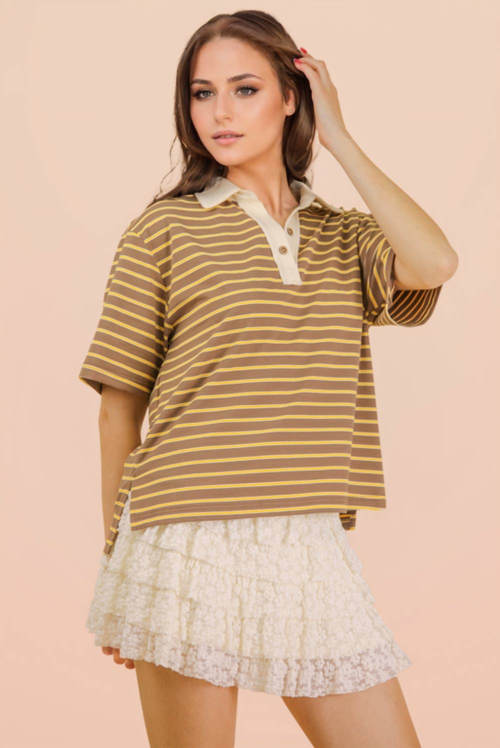 A woman wears a Mocha Oversized Stripe Knit Top in brown and yellow stripes with a cream-colored collar, paired with a white ruffled skirt.