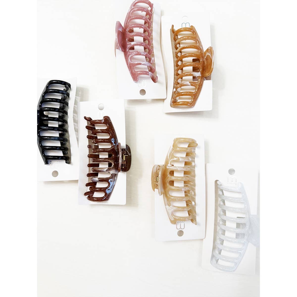Six Marbled Round Comb Hair Claw Clips by Love and Repeat—featured in black, brown, pink, caramel, light beige, and white—are displayed on individual white cards arranged on a white background.