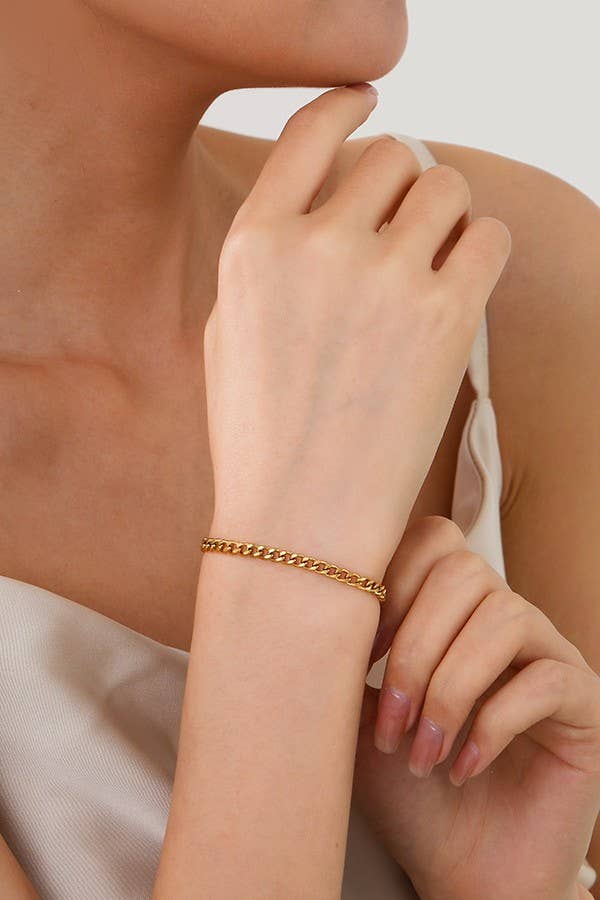 A person wearing the Dainty Gold Bracelet by JOSSLYN by wall to wall rests their hand near their chin. They are dressed in a white satin sleeveless top, with neatly manicured nails, set against a light and neutral background.