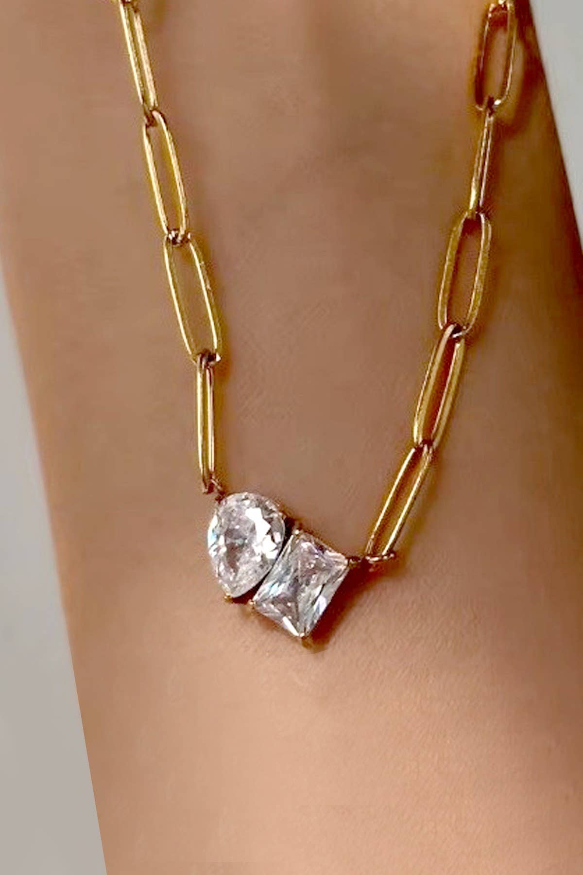 A gold Rhin Necklace from JOSSLYN by wall to wall, featuring two large gemstones—one oval and one square—set side by side.