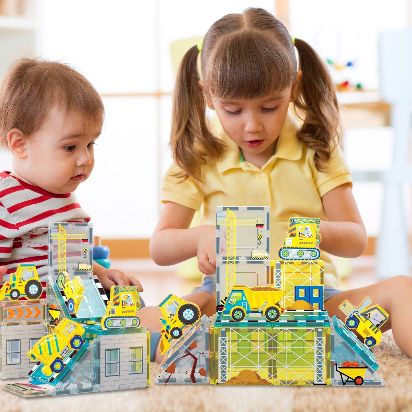 Two young children play indoors with the PicassoTiles 26 Piece Magnetic Building Set Playset by PicassoTiles, building colorful structures with magnetic tiles on a play mat.