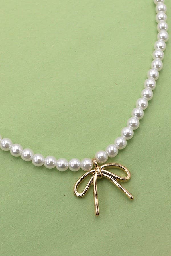 The JOSSLYN by wall to wall Pearl Chain Bow Charm Necklace is displayed on a light green background.