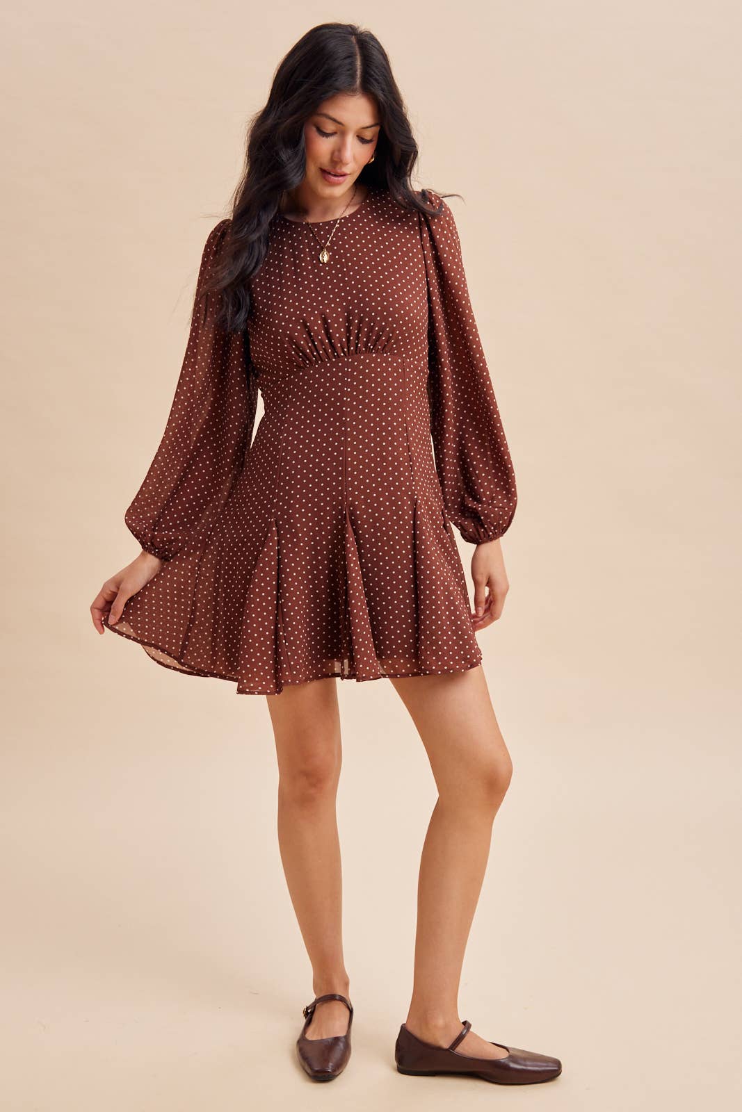 In Loom Polka Dot Flared Mini Dress in brown with white polka dots, featuring a gathered waist, flared skirt, and brown Mary Jane flats.