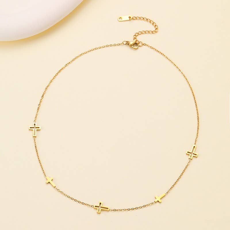 The Dainty Cross Necklace by JOSSLYN by wall to wall features five small cross charms evenly spaced along a fine gold chain, beautifully displayed on a light cream background.