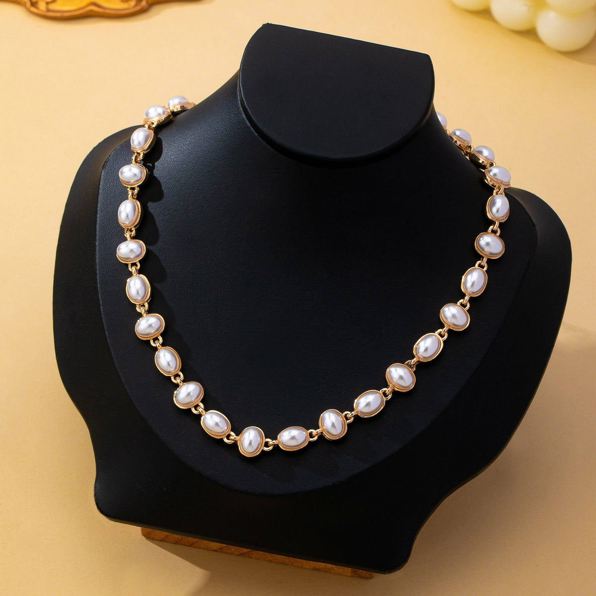 JOSSLYN by wall to wall Oval Pearl Link Necklace featuring a row of oval, white pearls set in gold-toned metal links, displayed on a black neck bust.