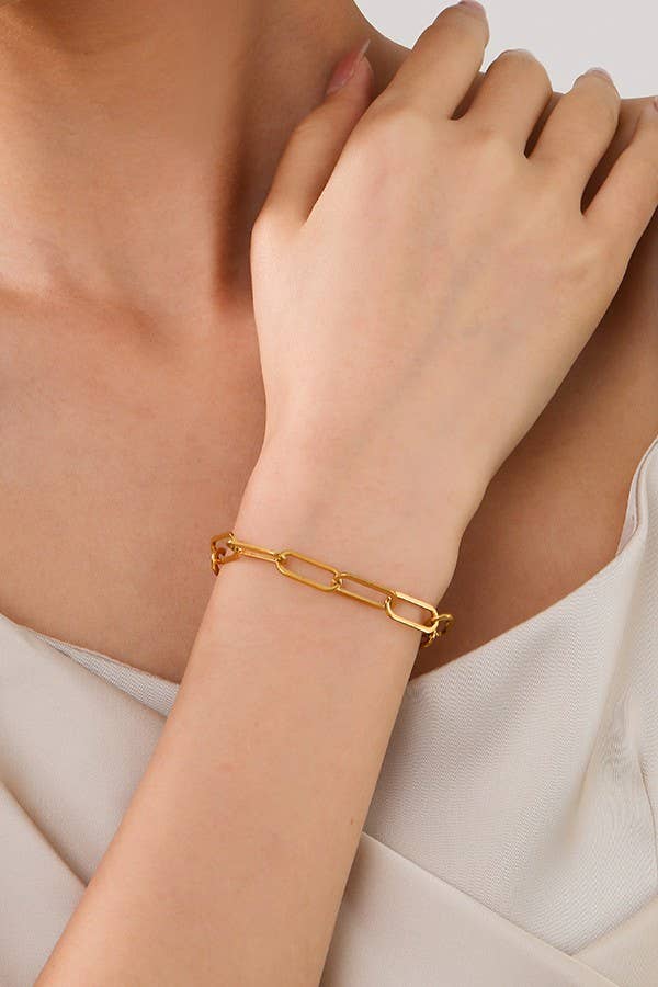 A person wearing the JOSSLYN by wall to wall Dainty Gold Bracelet on their wrist, dressed in a light-colored, sleeveless top.