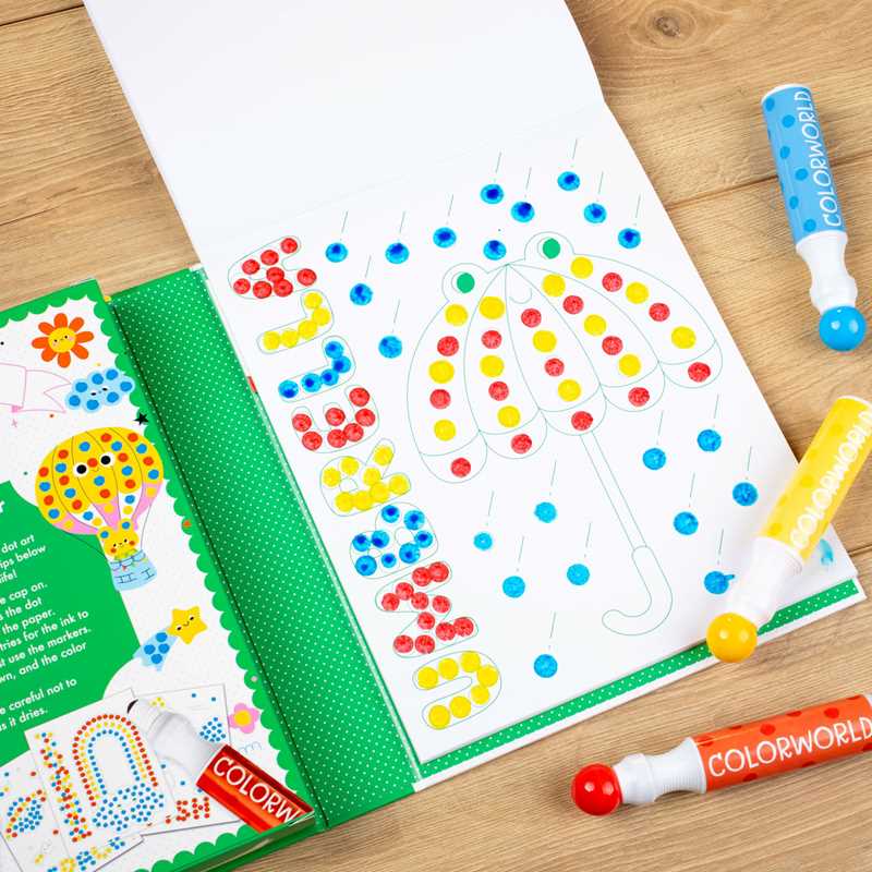 An open ColorWorld: Dot Art Fun Activity Book by Simon & Schuster lies on a wooden table, displaying dotted umbrella shapes partly filled with blue, yellow, orange, and red dot marker pens placed nearby.