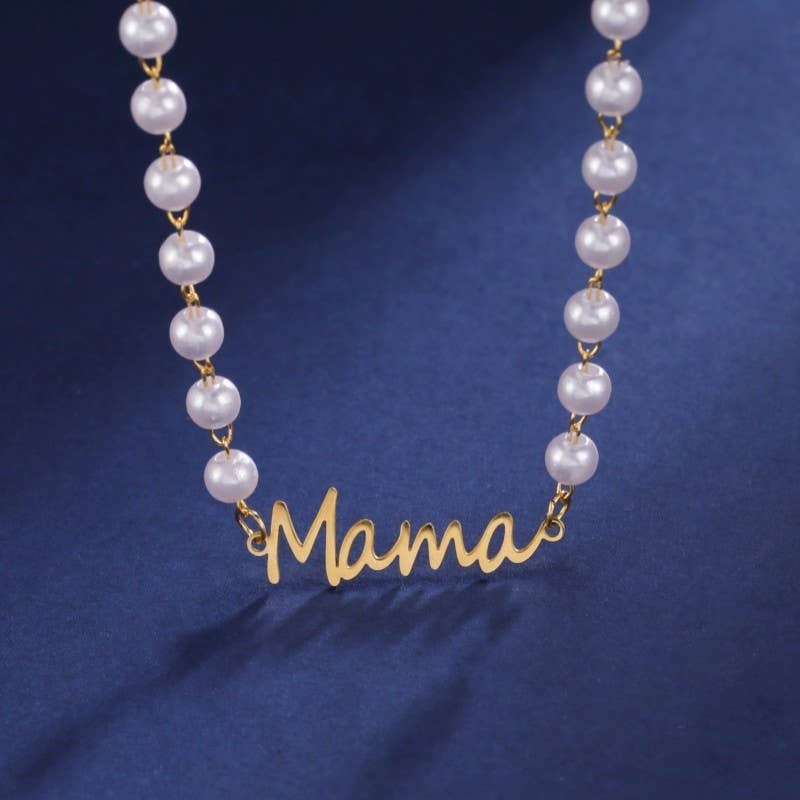 The Pearl Mama Necklace by JOSSLYN by wall to wall features white pearls forming the word “Mama” in cursive, elegantly displayed against a dark blue background.