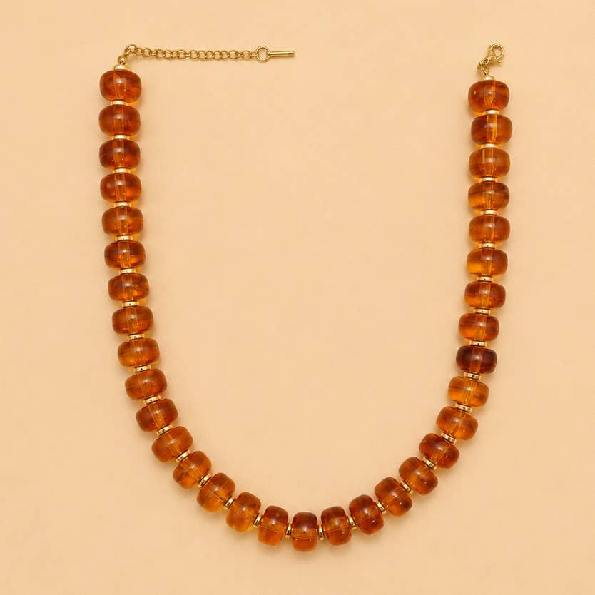 JOSSLYN by wall to wall Chunky Amber-Tone Barrel Bead Necklace featuring translucent amber-toned barrel beads separated by small gold-tone spacers with an adjustable gold-tone chain clasp.